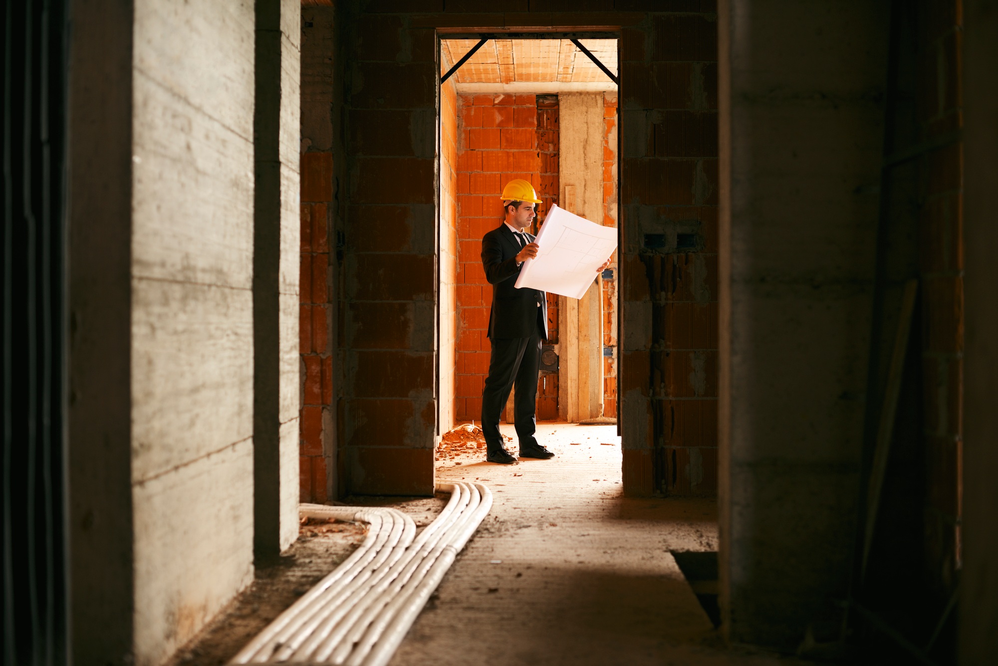 Architect Standing In House Under Construction With Plans