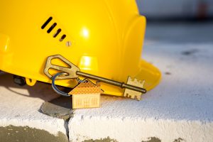 Construction yellow hardhat and key to house on window of housing made of blocks of porous concrete.